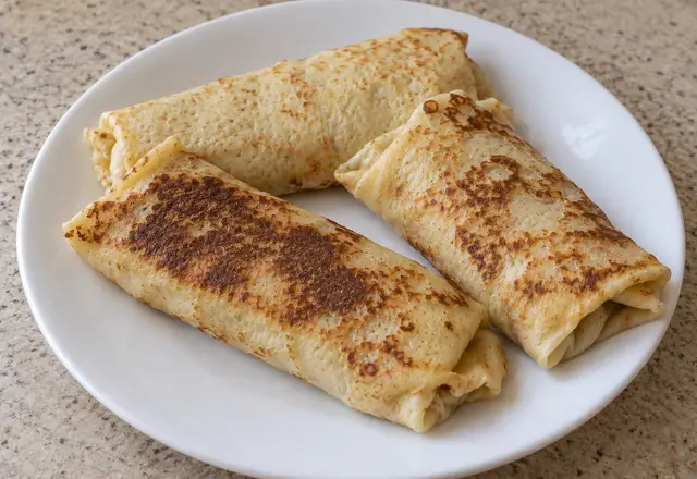 Three thin folded cheese blintzes with varied browning and slightly uneven tucked ends on a plain white plate